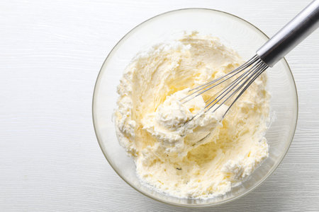 Bowl with whisk and whipped cream on white wooden table, top viewの写真素材