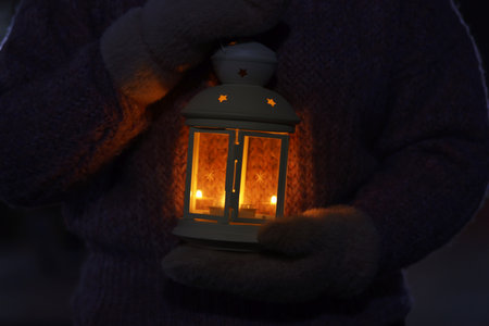 Woman holding Christmas lantern with burning candle in darkness, closeupの写真素材