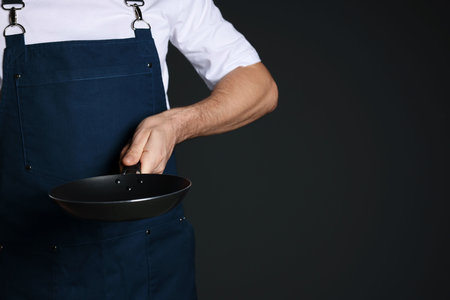 Chef holding frying pan on black background, closeup. Space for textの写真素材