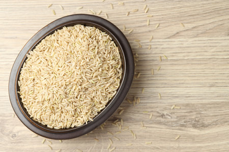 Brown rice in bowl on wooden table, top view. Space for textの写真素材
