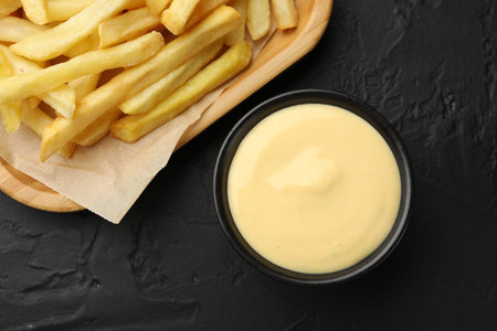 Tasty cheese sauce in bowl and French fries on black table, flat layの写真素材