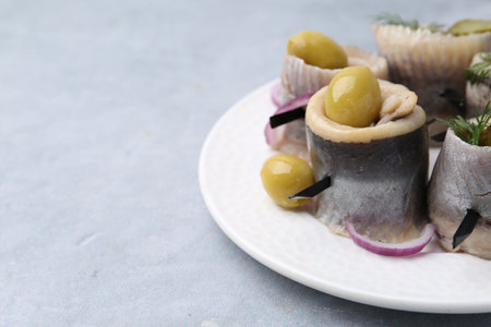 Delicious herring rolls with olives, pickles, dill and onion on gray table, closeup. Space for textの写真素材