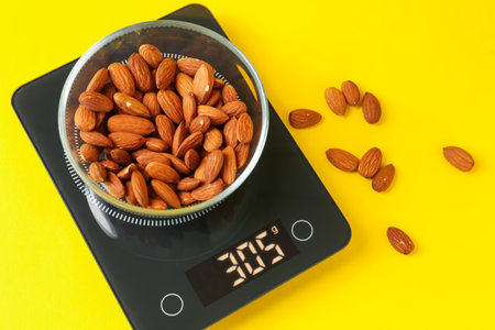Electronic kitchen scale with bowl of almond nuts on yellow background, flat layの写真素材