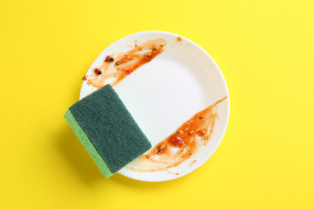 Dirty plate and sponge on yellow background, top viewの写真素材