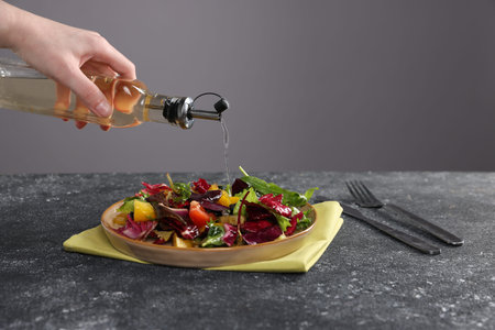 Woman pouring oil onto salad at dark textured table against gray background, closeupの写真素材