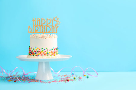 Delicious cake with colorful sprinkles, topper and serpentine streamer on light blue table. Space...