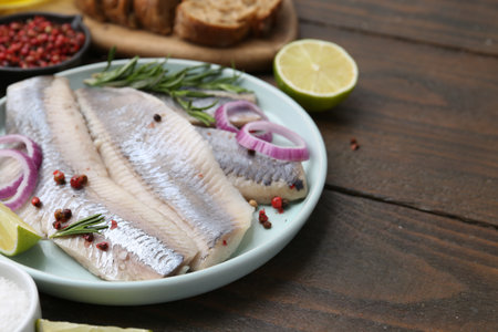 Marinated herring fillets with onion rings, rosemary, lime and peppercorns on wooden table, closeup. Space for textの写真素材