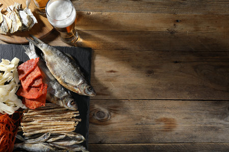 Dried fish and glass of beer on wooden table, flat lay. Space for text