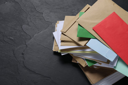 Post office. Stack of different paper envelopes on black table, above view. Space for text