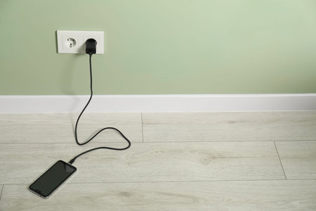 USB adapter with cable plugged into electric socket charging smartphone indoors. Space for text