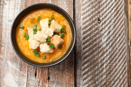 Tasty pumpkin cream soup with croutons and green onion in bowl on wooden table, top view. Space for textの写真素材