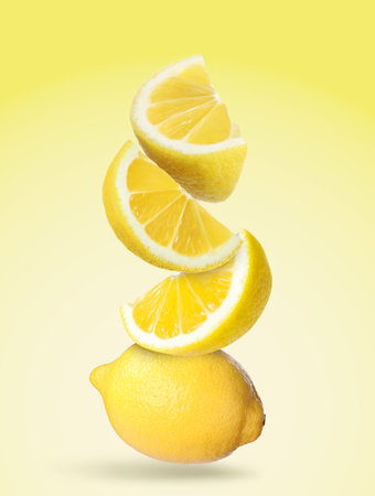 Cut and whole fresh lemons falling on yellow gradient backgroundの写真素材