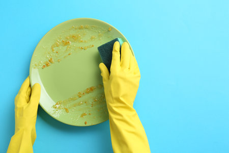 Man washing dirty plate with sponge on light blue background, top view. Space for textの写真素材