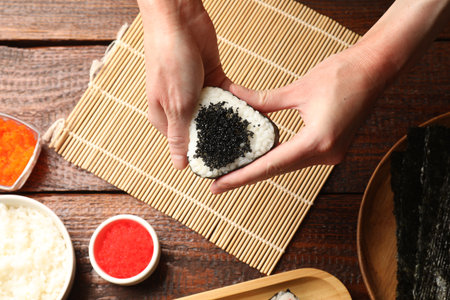 Woman with tobiko onigiri (Japanese rice ball) at wooden table, top viewの写真素材