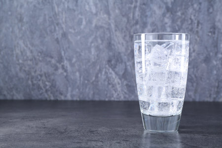 Refreshing soda water with ice cubes in glass on grey table, space for text