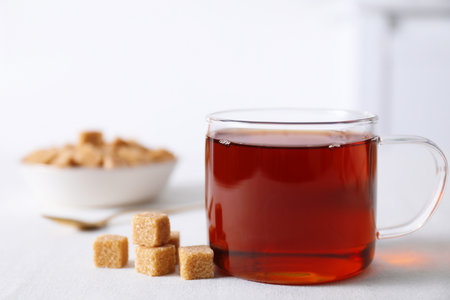 Aromatic black tea in cup and brown sugar cubes on white table, closeupの写真素材