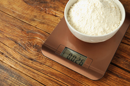 Modern electronic kitchen scale with bowl of flour on wooden table, closeup. Space for textの写真素材