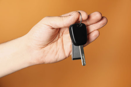 Man with car key and keychain on orange background, closeup