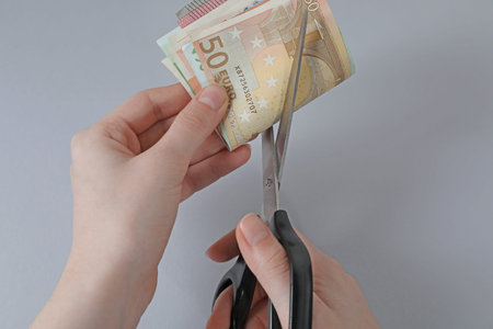 Woman cutting euro banknotes on gray background, closeup