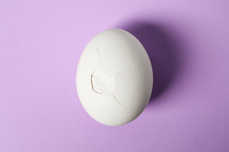 One egg with cracked shell on violet background, top viewの写真素材