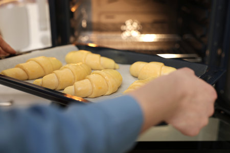 Woman putting baking sheet with raw croissants into oven, closeupの写真素材