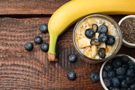 Delicious chia pudding with blueberries, banana and oatmeal in glass on wooden table, flat lay. Space for textの写真素材