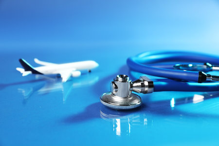 Stethoscope and airplane model on glass surface against blue background, closeupの写真素材