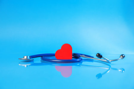 Stethoscope and red decorative heart on glass surface against light blue backgroundの写真素材