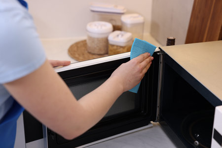 Woman cleaning microwave oven with rag indoors, closeup
