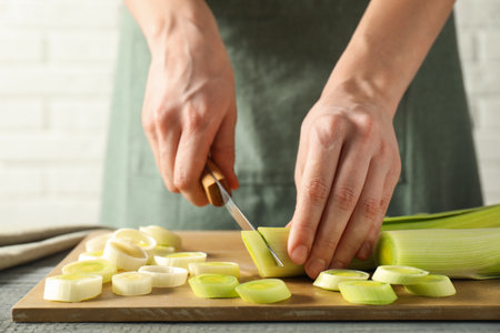 Woman cutting fresh leek at grey wooden table, closeupの写真素材