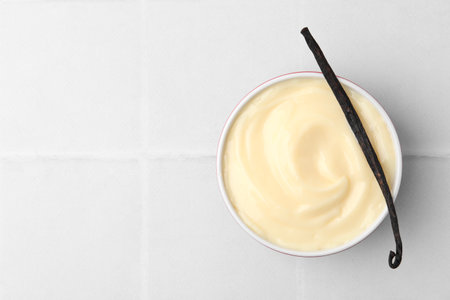 Tasty vanilla pudding and pod on white tiled table, top view. Space for textの写真素材
