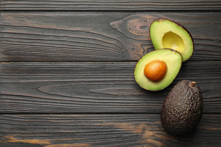 Whole and cut avocados on dark wooden table, flat lay. Space for textの写真素材