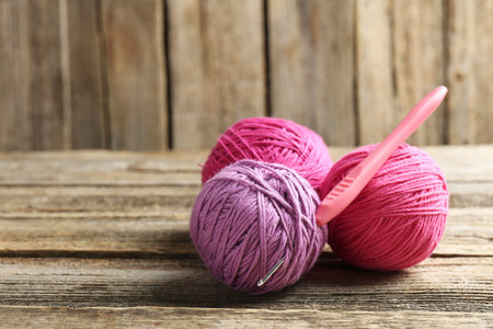 Balls of colorful yarn and crochet hook on wooden table, closeup. Space for textの写真素材