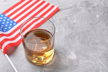 Glass of whiskey and American flag on grey table, closeup. Space for textの写真素材