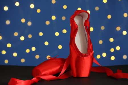 Pair of elegant pointe shoes on black table against blurred lightsの写真素材