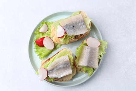 Tasty sandwiches with herring, radish and lettuce on light table, top viewの写真素材