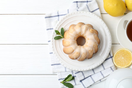 Delicious lemon cake with glaze, mint and citrus fruits on white wooden table, flat lay. Space for textの写真素材