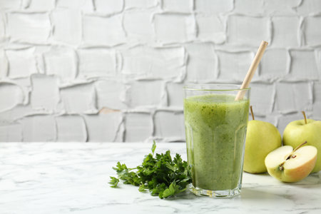 Healthy parsley smoothie in glass, leaves and apples on white marble table against gray textured background, closeup. Space for textの写真素材