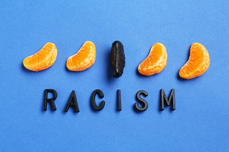 Word Racism and tangerine segments of different colors on blue background, flat lay