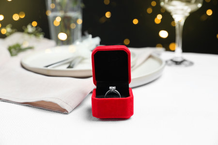 Engagement ring in box on white tablecloth, closeup. Romantic dinnerの写真素材