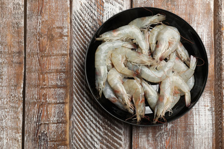 Fresh raw shrimps in bowl on wooden table, top view. Space for textの写真素材