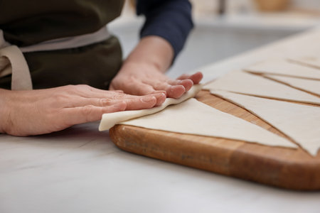 Woman rolling croissant from fresh dough at light table indoors, closeupの写真素材