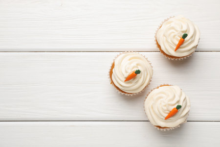 Tasty carrot muffins with cream on white wooden table, flat lay. Space for textの写真素材