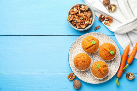Tasty carrot muffins, walnuts and fresh vegetables on light blue wooden table, flat lay. Space for textの写真素材