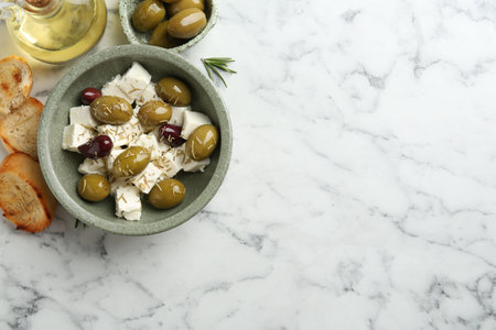 Marinated olives with feta cheese, bread pieces, oil and rosemary on white marble table, flat lay. Space for textの写真素材