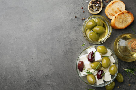 Tasty olives served with feta cheese, bread and oil on grey textured table, flat lay. Space for textの写真素材