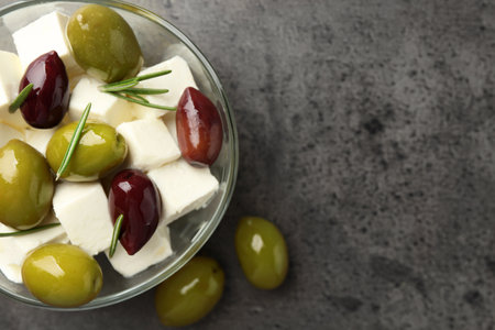 Tasty olives with feta cheese in glass bowl on grey textured table, top view. Space for textの写真素材