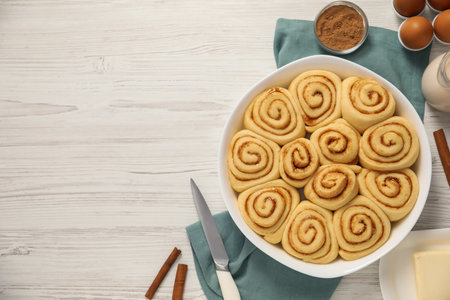 Raw cinnamon rolls and different ingredients on light wooden table, flat lay. Space for textの写真素材