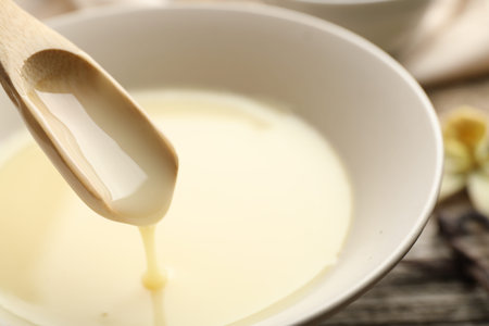Taking tasty vanilla condensed milk with spoon from bowl on table, closeupの写真素材