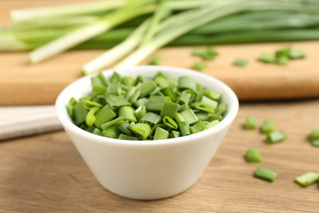 Cut fresh green onions in bowl on wooden table, closeupの写真素材